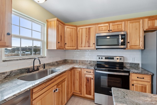 kitchen with sink, appliances with stainless steel finishes, light stone countertops, light hardwood / wood-style floors, and decorative backsplash