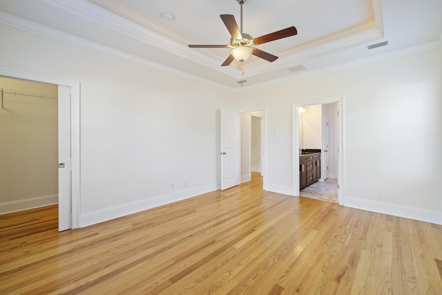 unfurnished bedroom with a closet, ceiling fan, a tray ceiling, crown molding, and light hardwood / wood-style flooring