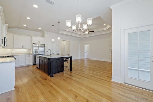 kitchen with sink, a center island with sink, stainless steel fridge, pendant lighting, and white cabinets