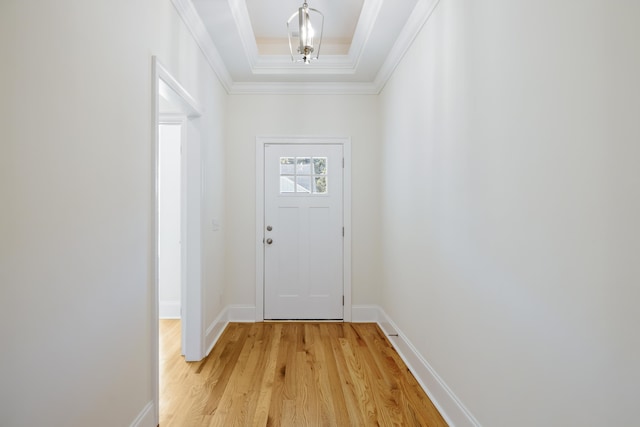 doorway with a tray ceiling, ornamental molding, and light wood-type flooring