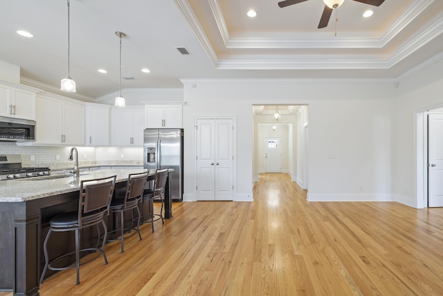 kitchen with appliances with stainless steel finishes, a tray ceiling, pendant lighting, light stone countertops, and white cabinets