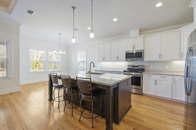 kitchen with white cabinetry, hanging light fixtures, stainless steel appliances, and an island with sink