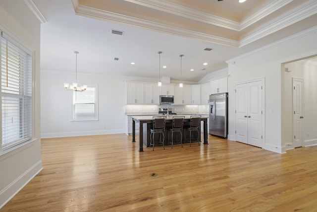 kitchen with decorative light fixtures, an island with sink, white cabinetry, a kitchen bar, and stainless steel appliances