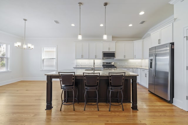 kitchen with a kitchen island with sink, white cabinetry, stainless steel appliances, tasteful backsplash, and decorative light fixtures