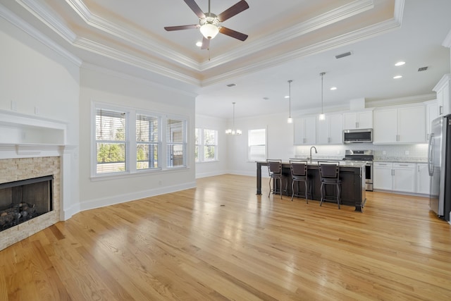 kitchen featuring a kitchen bar, hanging light fixtures, an island with sink, stainless steel appliances, and white cabinets