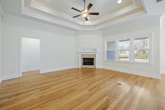 unfurnished living room featuring a tray ceiling, a fireplace, ceiling fan, and light wood-type flooring