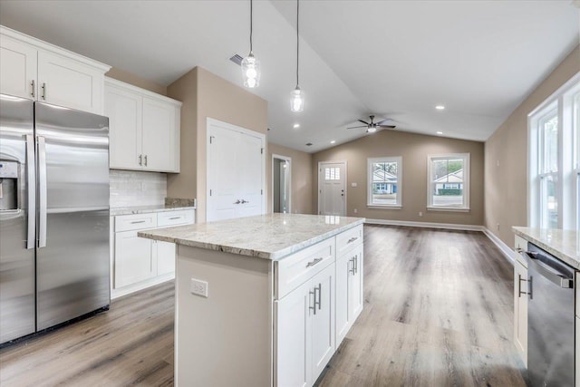 kitchen with pendant lighting, appliances with stainless steel finishes, a center island, white cabinets, and vaulted ceiling