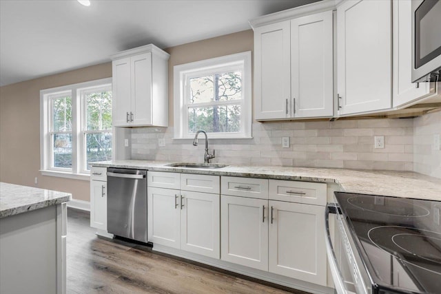 kitchen with white cabinetry, sink, backsplash, stainless steel appliances, and light wood-type flooring