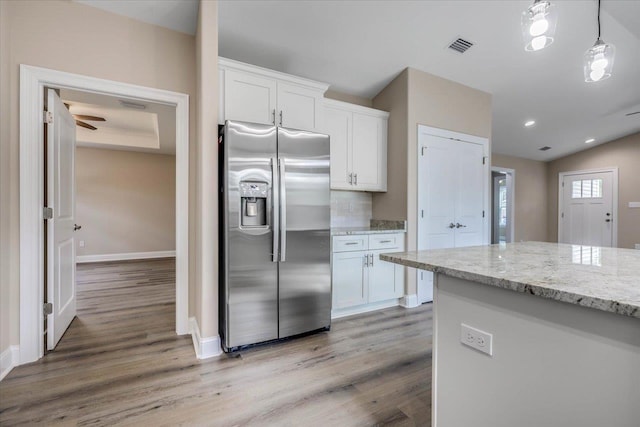 kitchen featuring stainless steel refrigerator with ice dispenser, white cabinetry, light stone counters, and pendant lighting