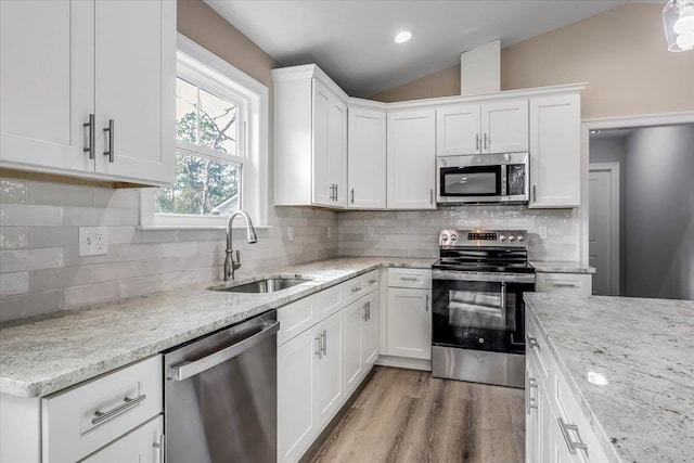 kitchen featuring white cabinetry, lofted ceiling, sink, stainless steel appliances, and light stone countertops