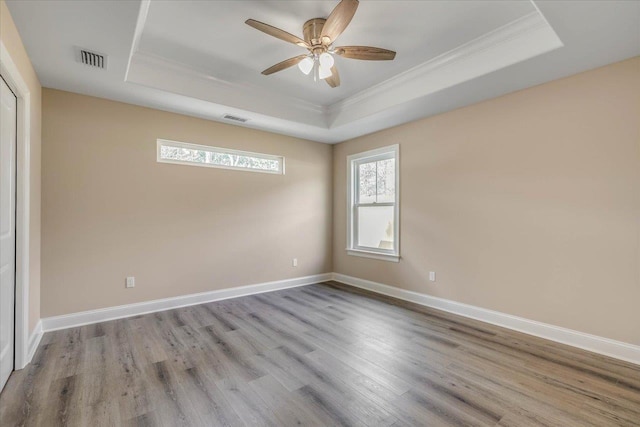 empty room featuring ornamental molding, light hardwood / wood-style floors, a raised ceiling, and ceiling fan