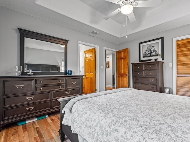 bedroom featuring ceiling fan, light wood-type flooring, and a tray ceiling