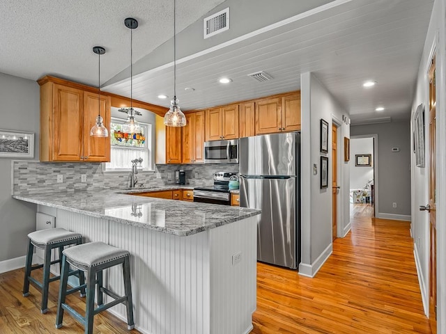 kitchen with kitchen peninsula, stainless steel appliances, light stone counters, and tasteful backsplash