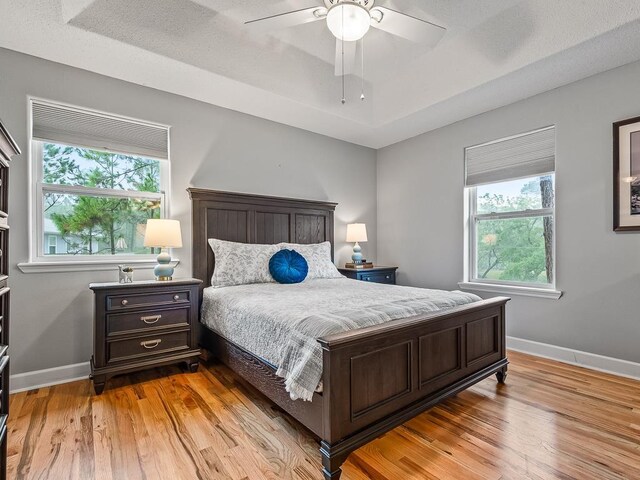 bedroom with a raised ceiling, ceiling fan, light hardwood / wood-style floors, and a textured ceiling