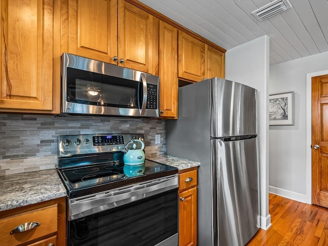 kitchen with decorative backsplash, light stone counters, light hardwood / wood-style flooring, and appliances with stainless steel finishes