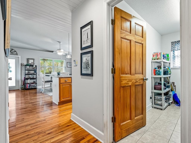 hallway featuring a textured ceiling, vaulted ceiling, and light tile patterned flooring