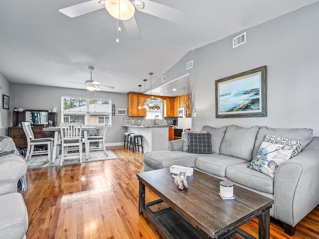 living room featuring ceiling fan, light wood-type flooring, sink, and lofted ceiling