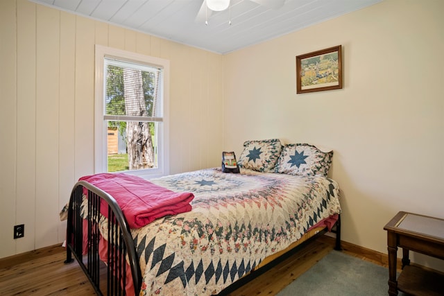 bedroom with dark hardwood / wood-style flooring, wooden walls, and ceiling fan