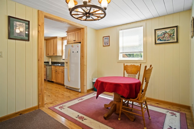 dining room featuring light wood-type flooring, wooden walls, and an inviting chandelier