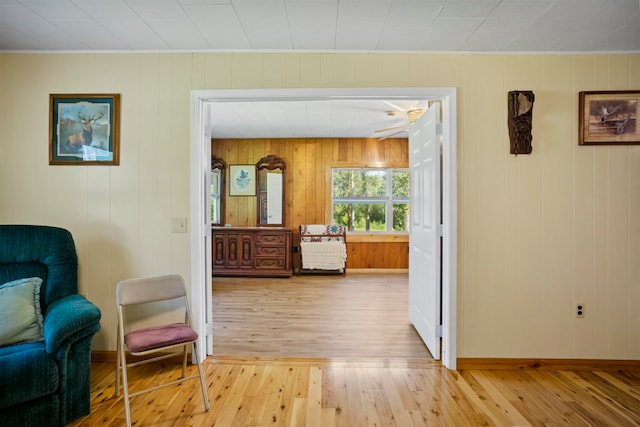 sitting room with light wood-type flooring, wooden walls, and ceiling fan