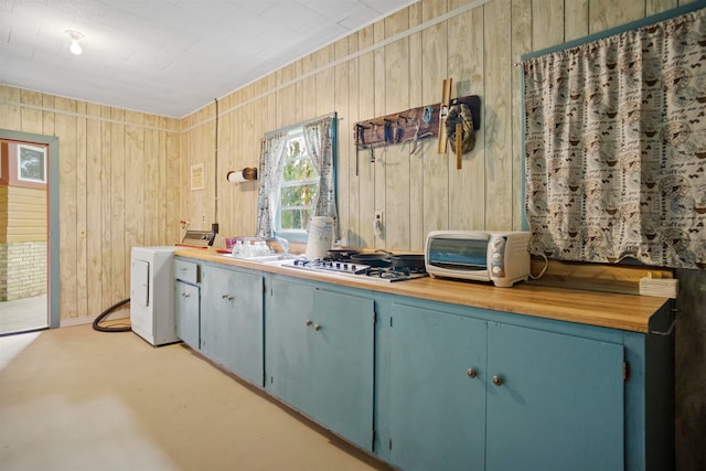 kitchen featuring wood walls, washer / dryer, and stainless steel gas stovetop