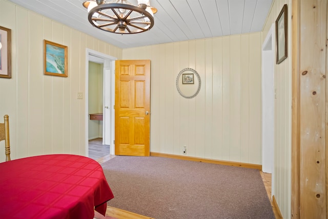 bedroom featuring carpet, wood walls, and an inviting chandelier