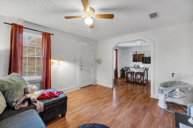 living room with light wood finished floors, baseboards, visible vents, arched walkways, and a textured ceiling