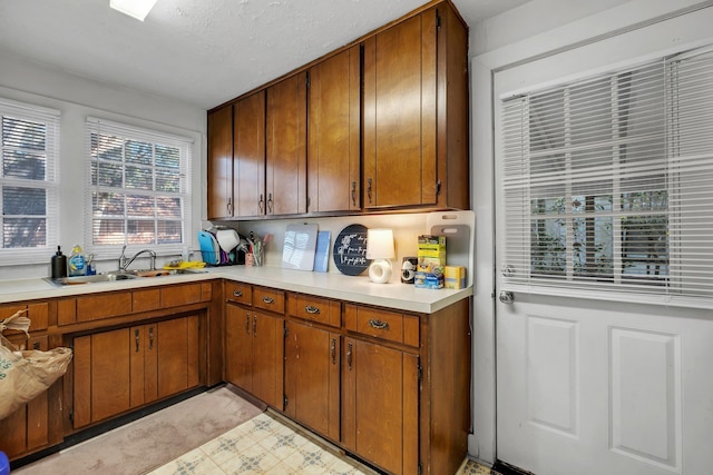 kitchen with light countertops, brown cabinetry, a sink, and light floors