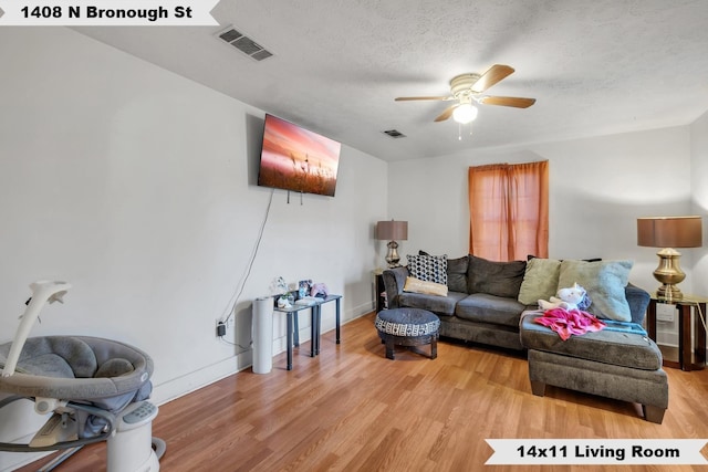 living room featuring light wood finished floors, ceiling fan, visible vents, and a textured ceiling