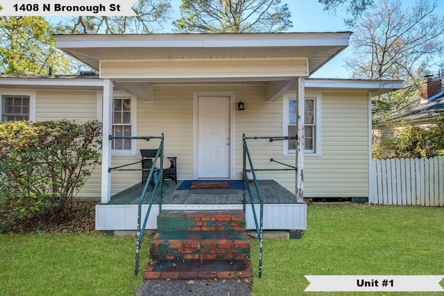 doorway to property featuring a porch, a lawn, and fence