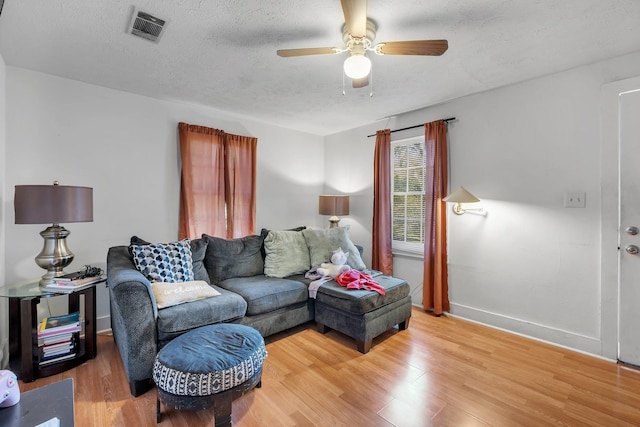 living room featuring a textured ceiling, ceiling fan, light wood finished floors, and visible vents