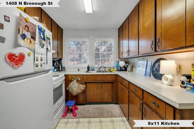 kitchen featuring light floors, light countertops, brown cabinetry, a sink, and white appliances