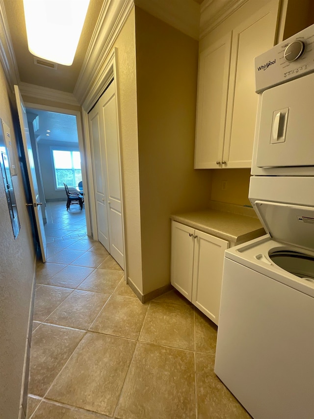 laundry room featuring cabinets, light tile patterned floors, stacked washer and dryer, and crown molding