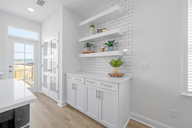 bar with white cabinets, light hardwood / wood-style floors, and backsplash