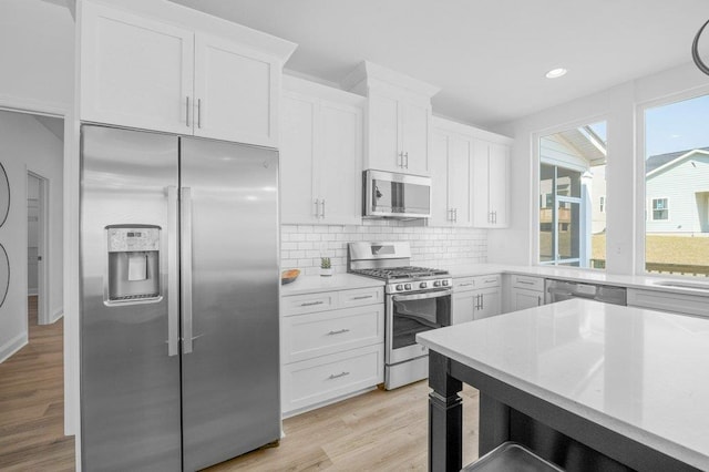 kitchen featuring white cabinetry, decorative backsplash, stainless steel appliances, and light hardwood / wood-style flooring