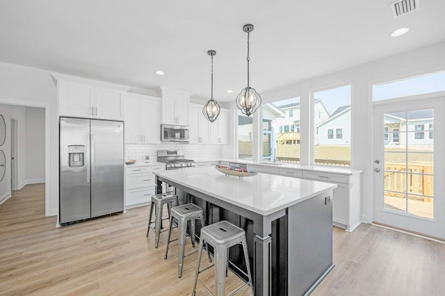 kitchen with stainless steel appliances, light wood-type flooring, a breakfast bar, white cabinets, and a center island