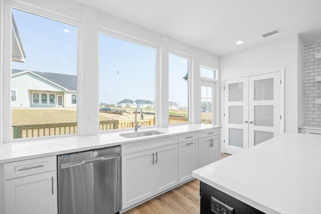 kitchen featuring light hardwood / wood-style floors, sink, tasteful backsplash, stainless steel dishwasher, and white cabinetry