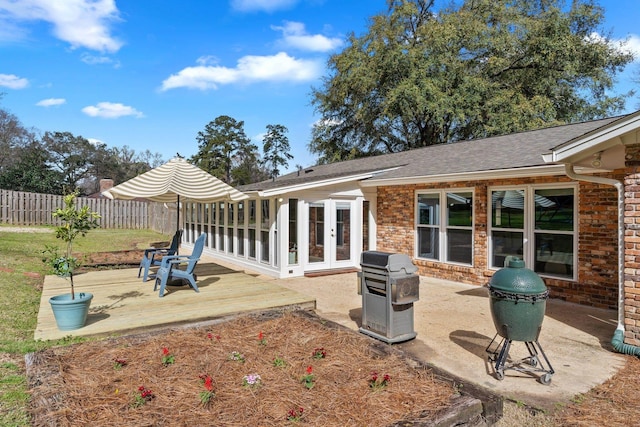 rear view of property with a deck, french doors, brick siding, and fence