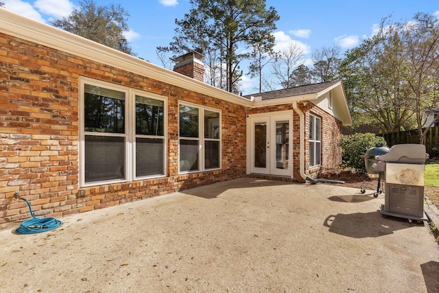 back of house featuring brick siding, a patio area, a chimney, and french doors