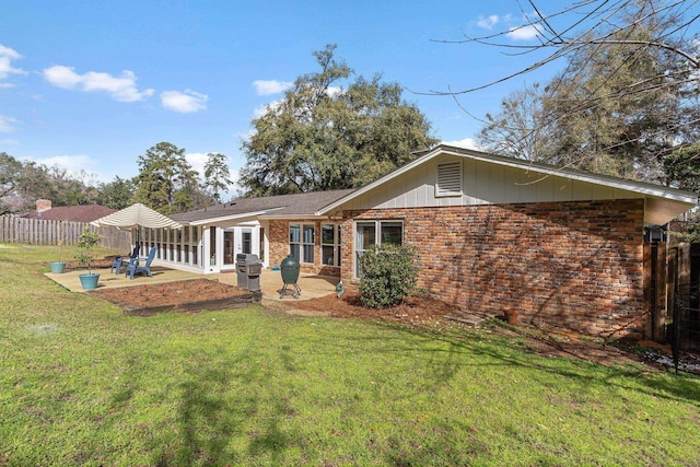 rear view of house featuring brick siding, fence, a lawn, and a patio