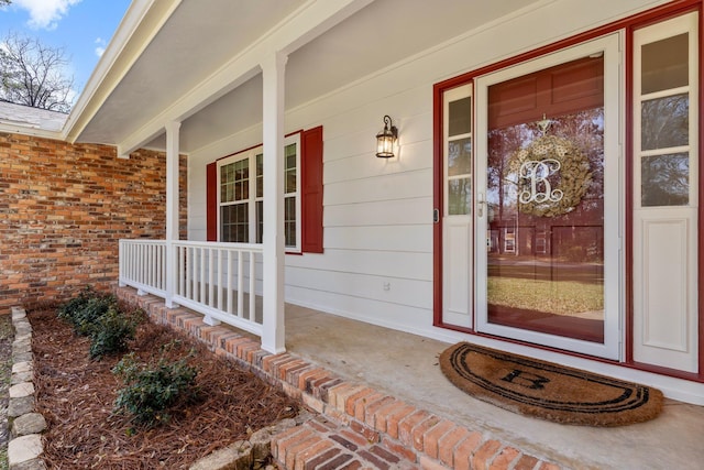 entrance to property featuring a porch and brick siding