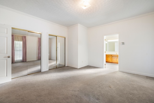 unfurnished bedroom with multiple closets, connected bathroom, light colored carpet, and crown molding