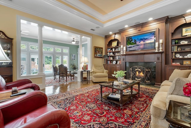 living room featuring ornate columns, ornamental molding, ceiling fan, a premium fireplace, and built in shelves