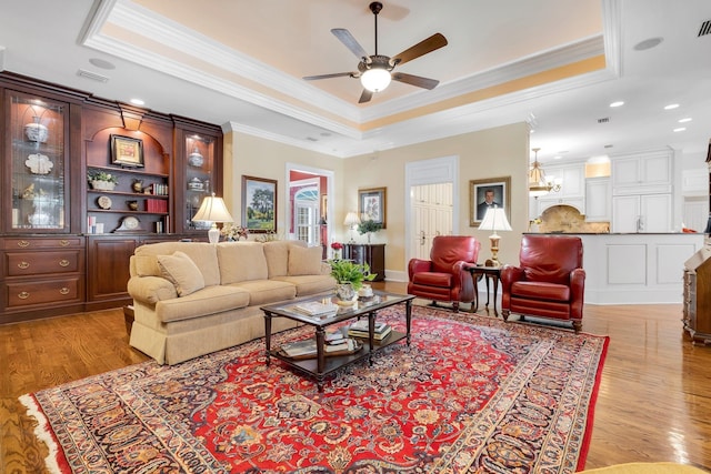 living room featuring a tray ceiling, ornamental molding, light hardwood / wood-style floors, and ceiling fan