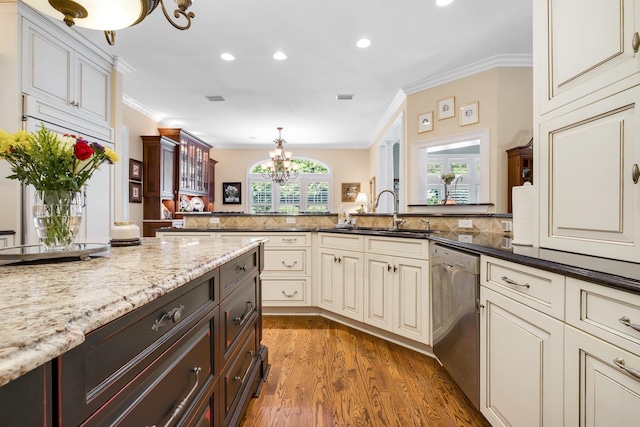 kitchen featuring sink, dark stone countertops, ornamental molding, stainless steel dishwasher, and a notable chandelier