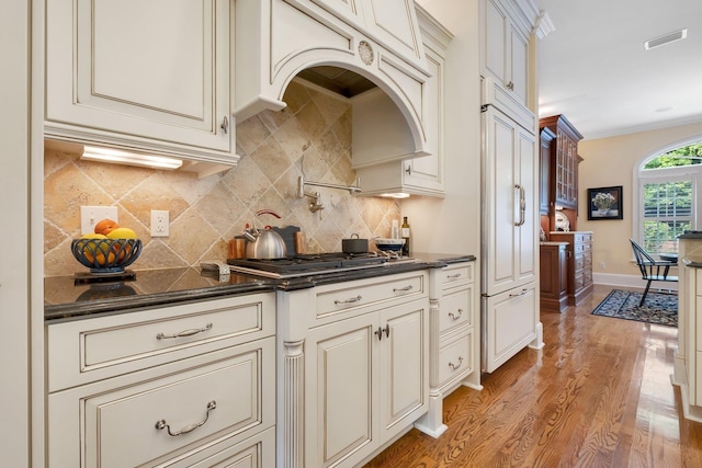 kitchen featuring light hardwood / wood-style flooring, ornamental molding, paneled built in fridge, stainless steel gas stovetop, and backsplash