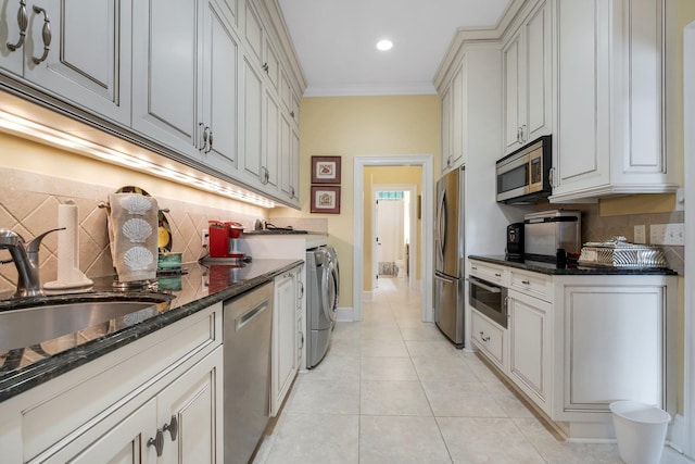 kitchen featuring sink, dark stone counters, light tile patterned floors, stainless steel appliances, and washer and clothes dryer