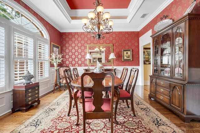 dining area with ornamental molding, a tray ceiling, a notable chandelier, and light hardwood / wood-style flooring