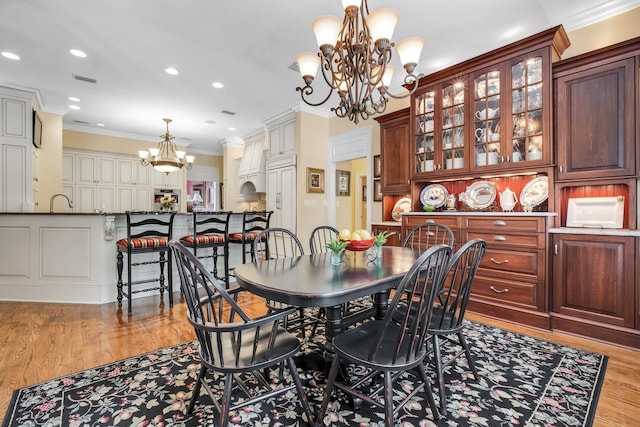 dining area with an inviting chandelier, crown molding, sink, and light hardwood / wood-style flooring