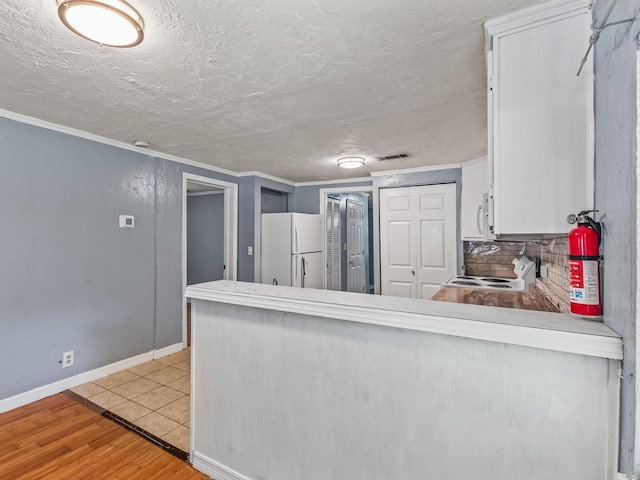 1487 Bainbridge Hwy, Quincy, FL 32352 - kitchen featuring freestanding refrigerator, range, a peninsula, white cabinetry, and ornamental molding